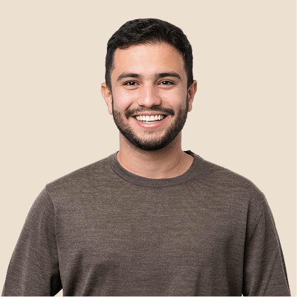 Smiling young man with short black hair, a beard, and wearing a brown shirt against a neutral background.