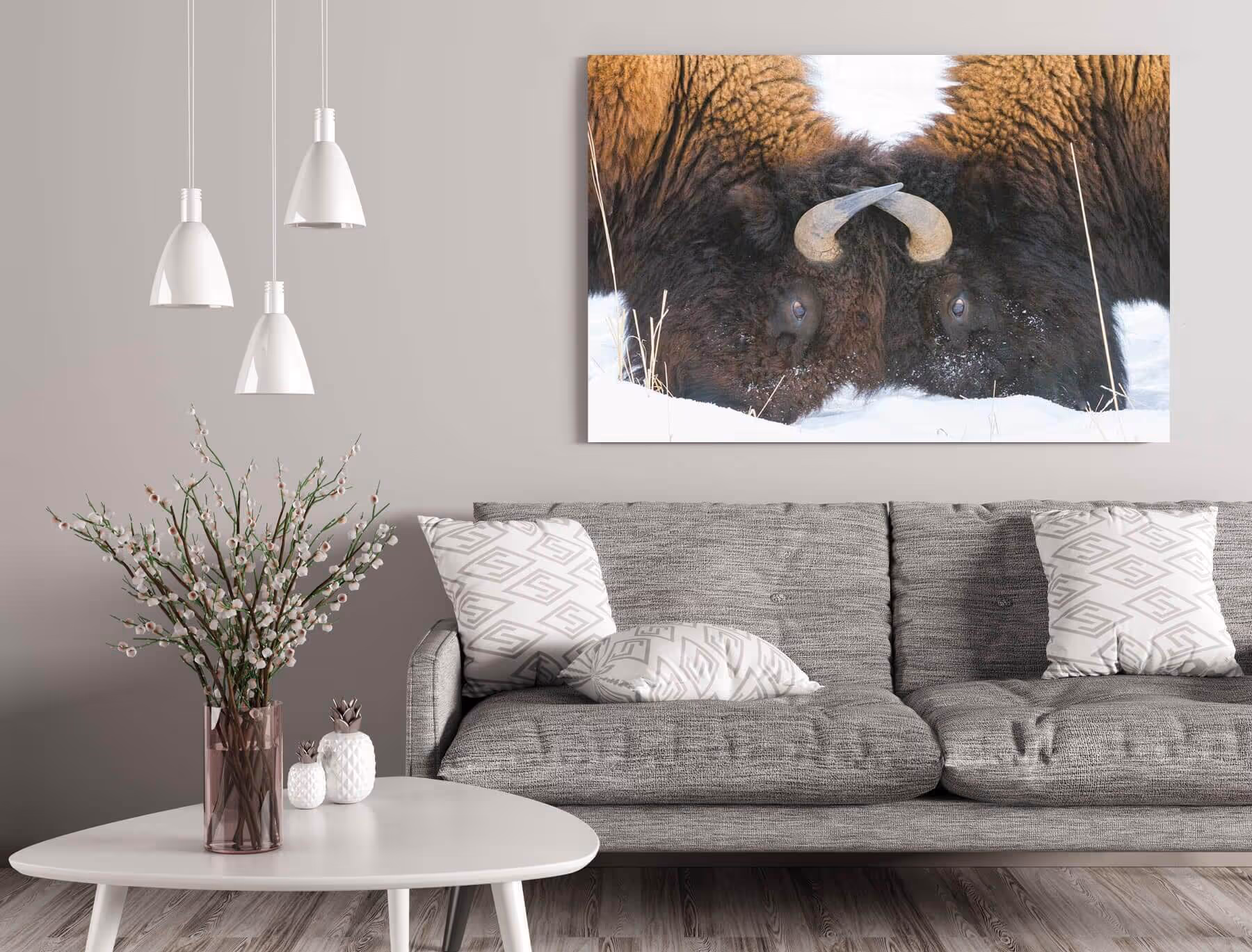 Modern living room with a gray sofa, patterned pillows, a white coffee table with a vase of flowers, and a large wall art print of a bison's face in snow.