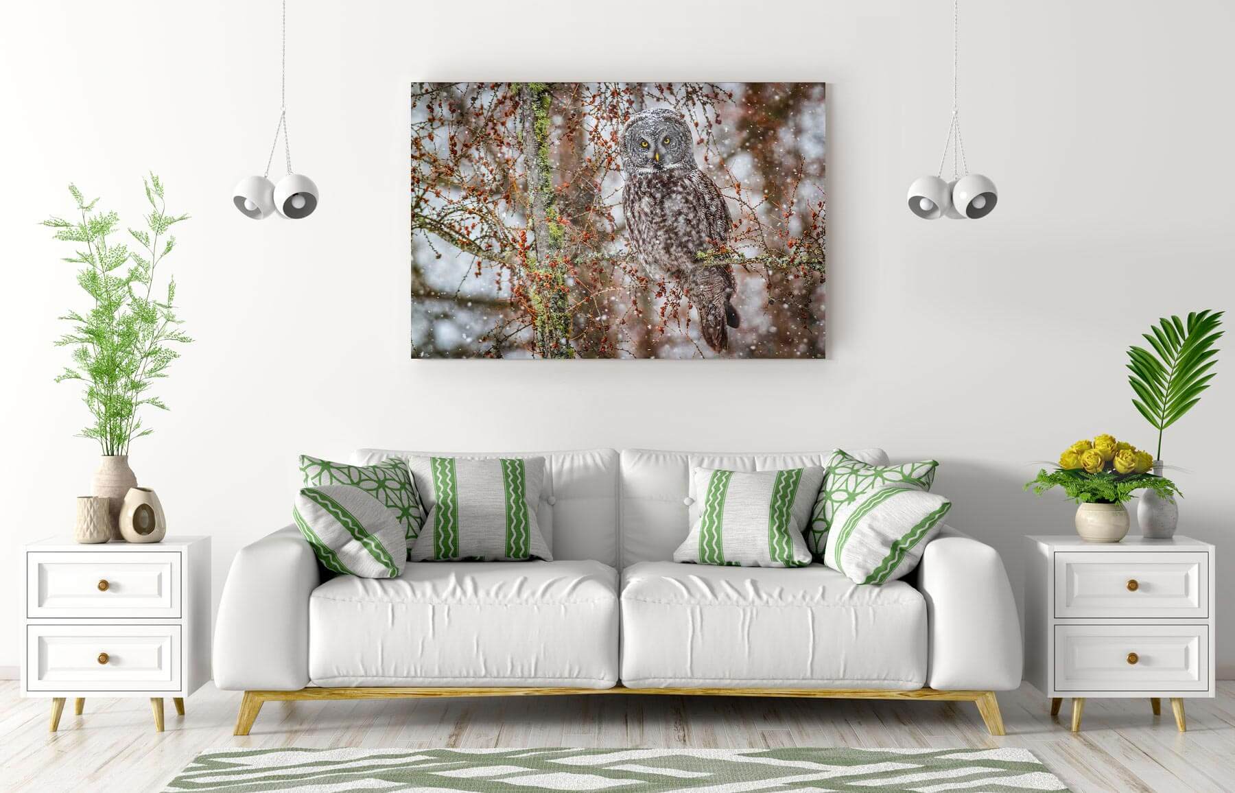 Modern white living room with a white sofa featuring green and white cushions, two white side tables with plants and decor, and a large wall art of a grey owl perched on a snowy tree branch.