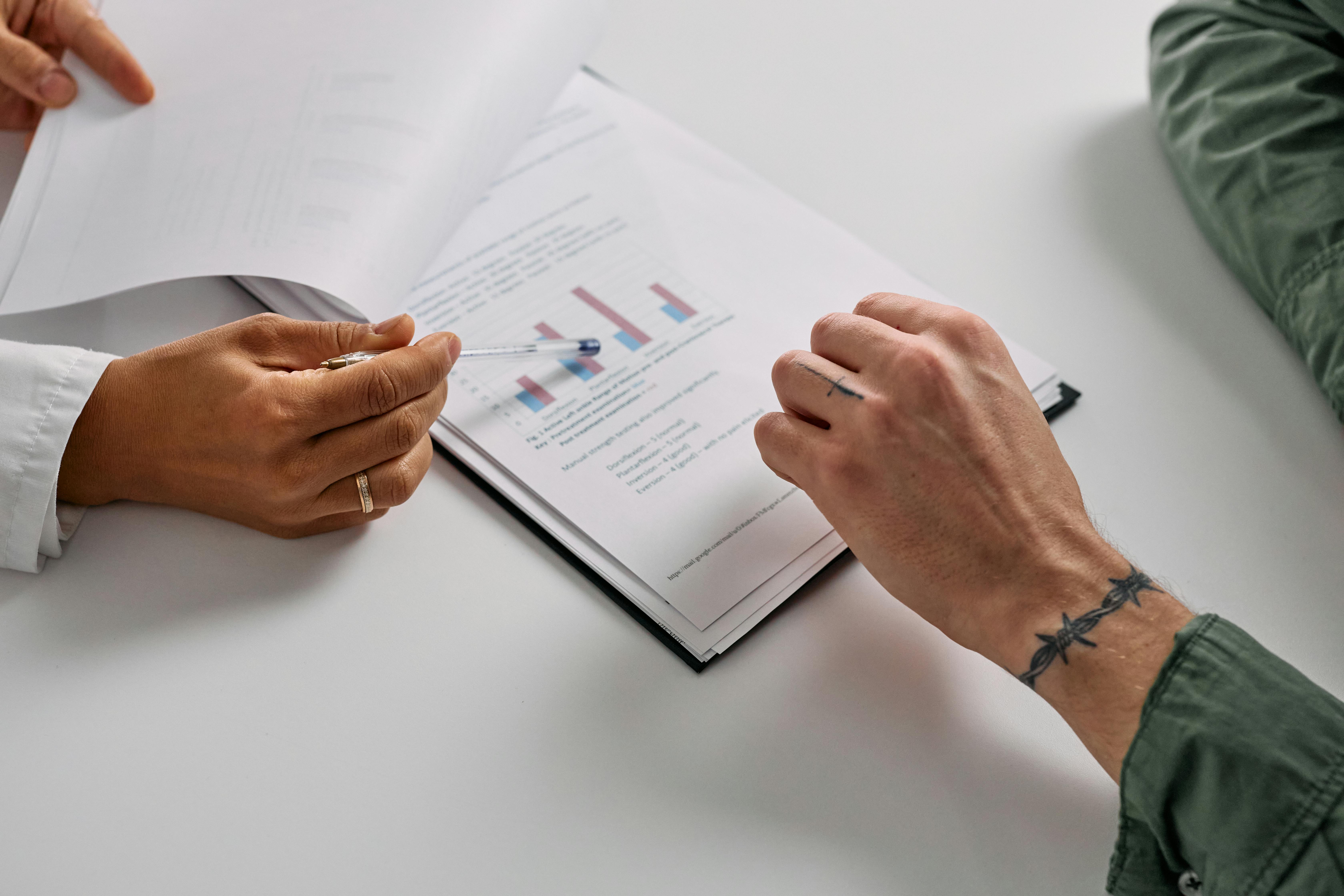Close-up of two people reviewing documents; one person points with a pen to graphs on the papers.
