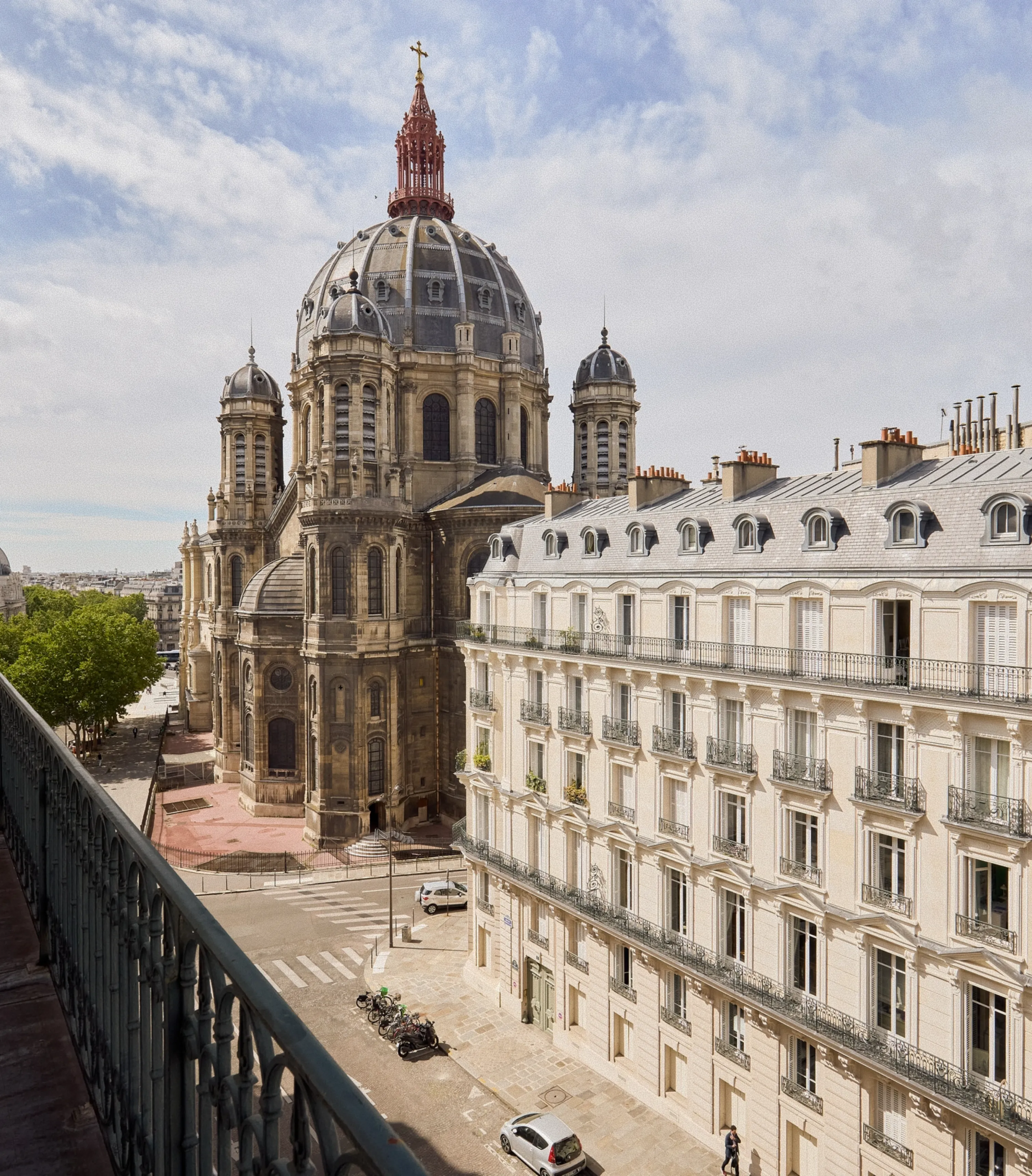 View of a historic domed church and adjacent classic Parisian apartment buildings under a partly cloudy sky.