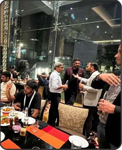 Group of men engaged in conversation and dining at a restaurant with large glass windows at night.
