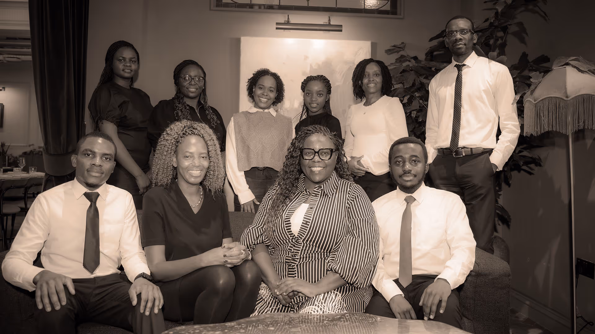 Group portrait of eleven professionally dressed individuals, sitting and standing in a warmly lit indoor setting.