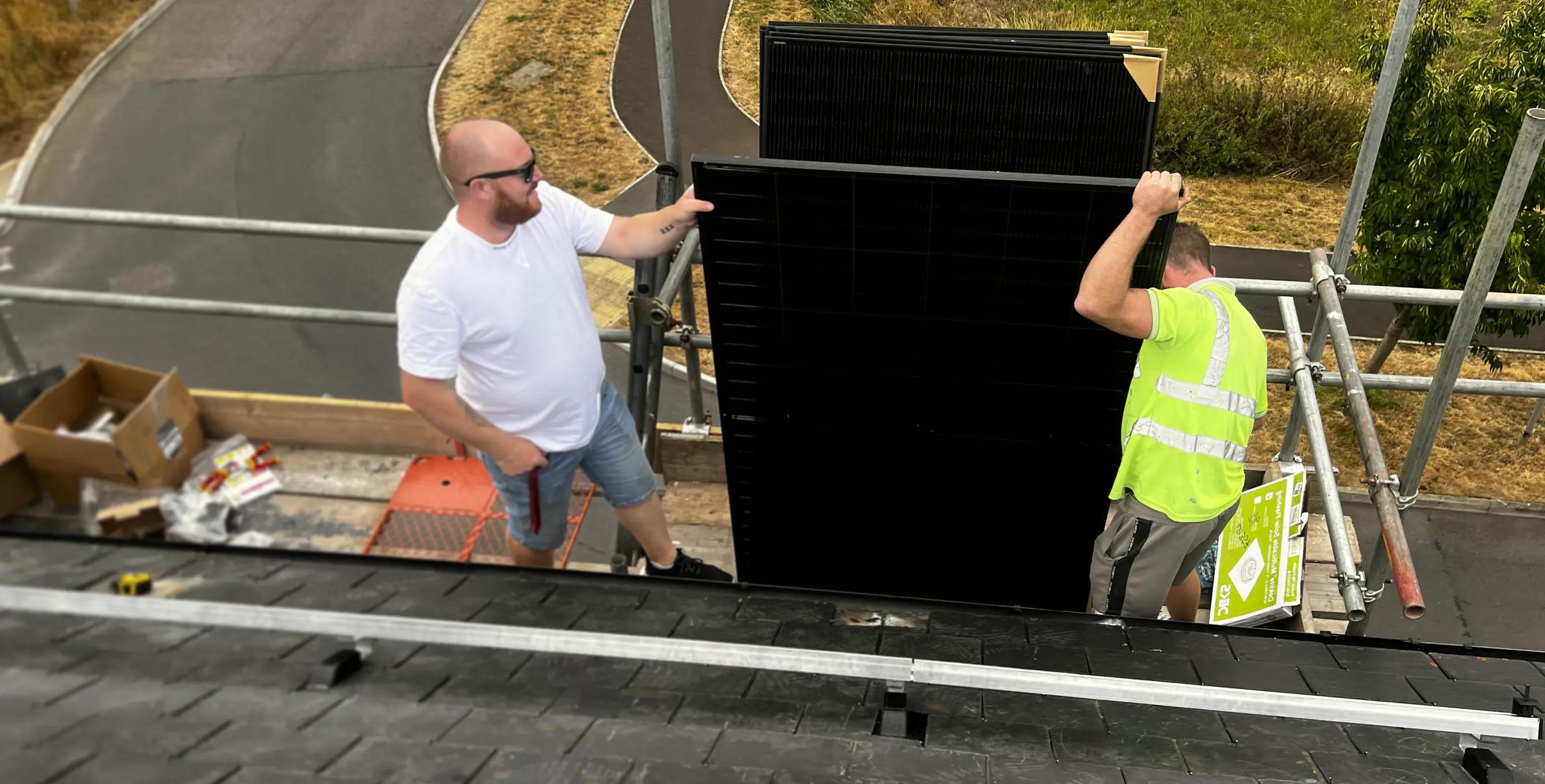 Two men on scaffolding installing large black solar panels on a rooftop.