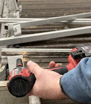 Close-up of a hand using a red power drill on a metal frame with a blue sleeve visible.