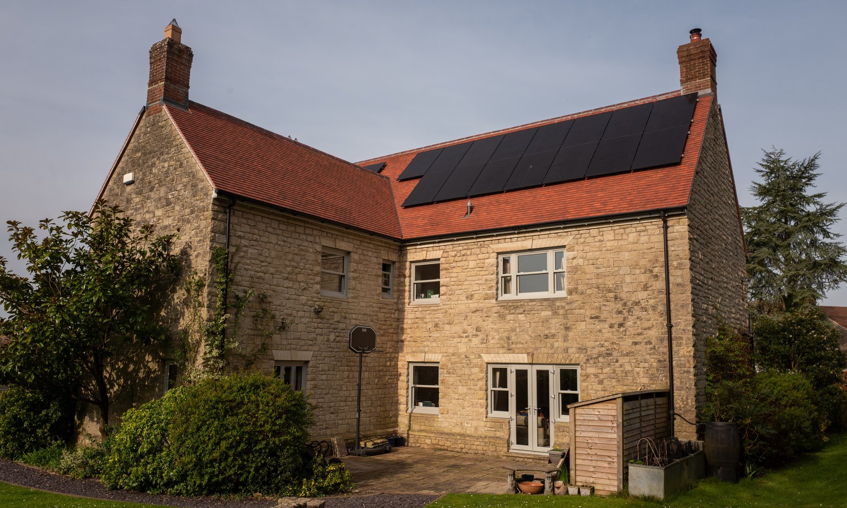 Black solar panels on the red tiled roof of a stone house, installed by JellyWatt