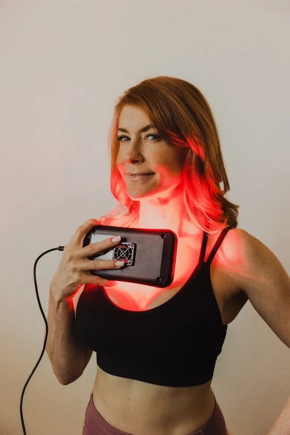 Woman in a black sports bra holding a device emitting red light to her neck area, showcasing LZR UltraBright technology