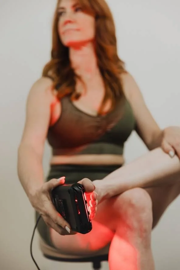 A person applying a device with red light therapy to their leg while seated, wearing athletic attire.