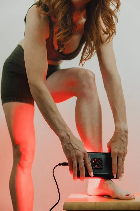 A person uses a device emitting red light on their foot while standing on a platform, focused on health or wellness treatment.