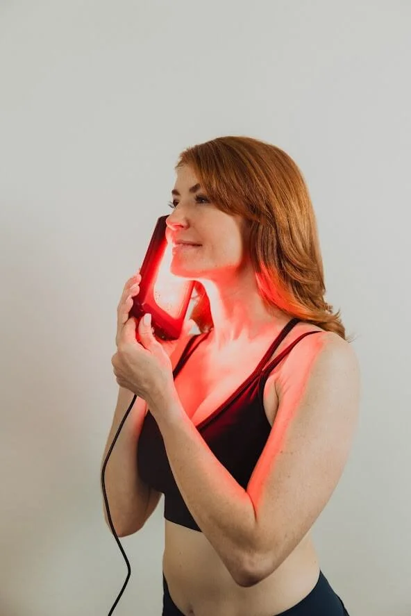 A woman with red hair uses a handheld red light therapy device on her face, promoting LZR UltraBright treatment.