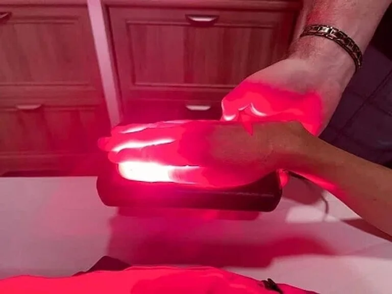 Hands grasping a device emitting red light, highlighting the palms against a blurred background.