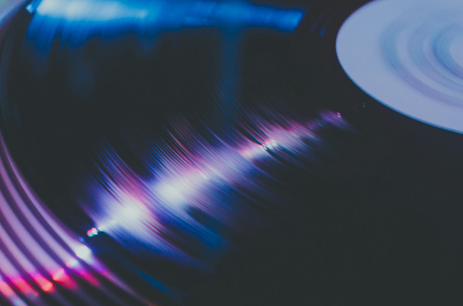 Close-up of a vinyl record with neon pink and blue light reflections.
