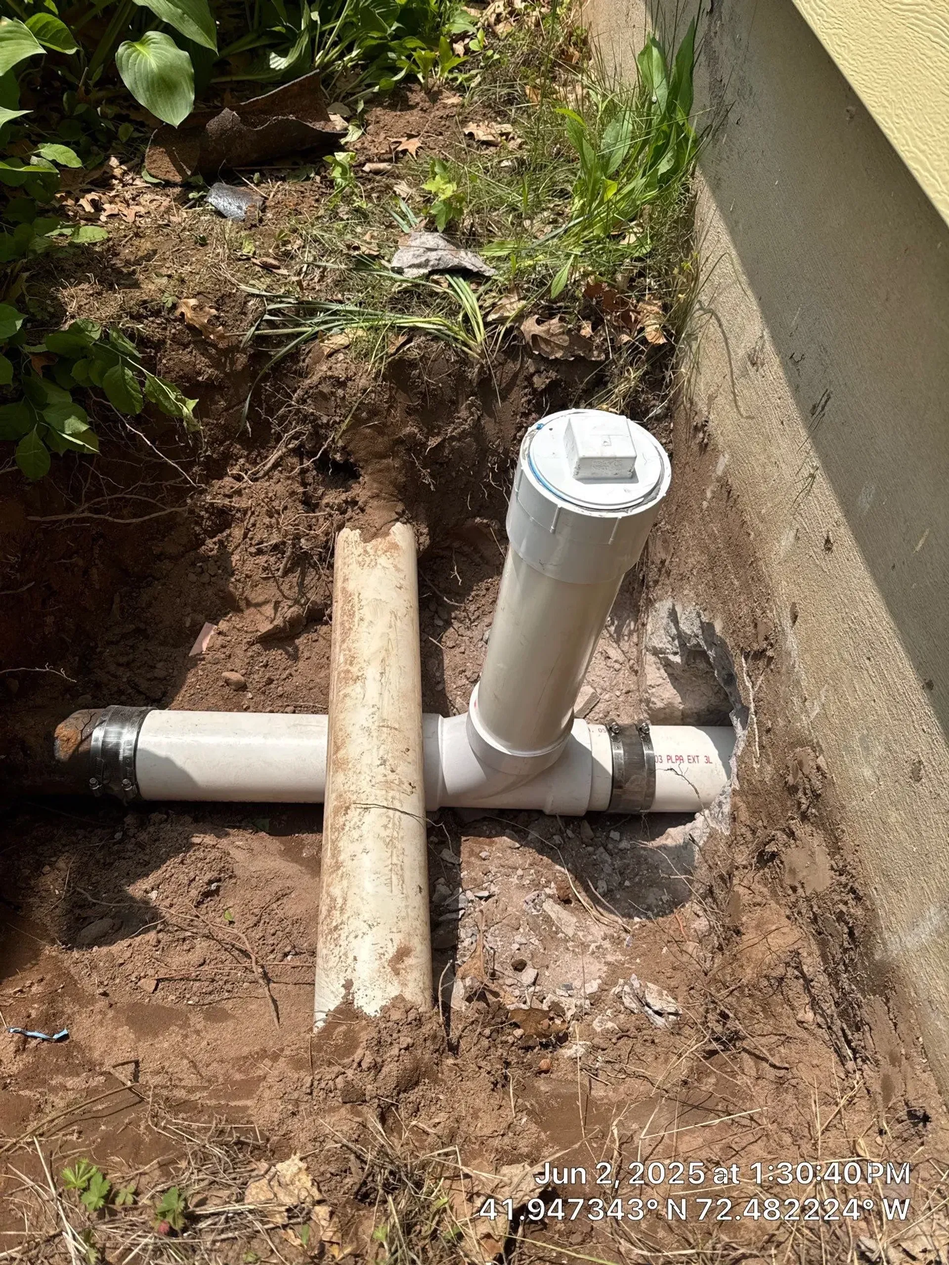 Exposed section of yard with newly installed PVC sewer cleanout and connected drain pipes