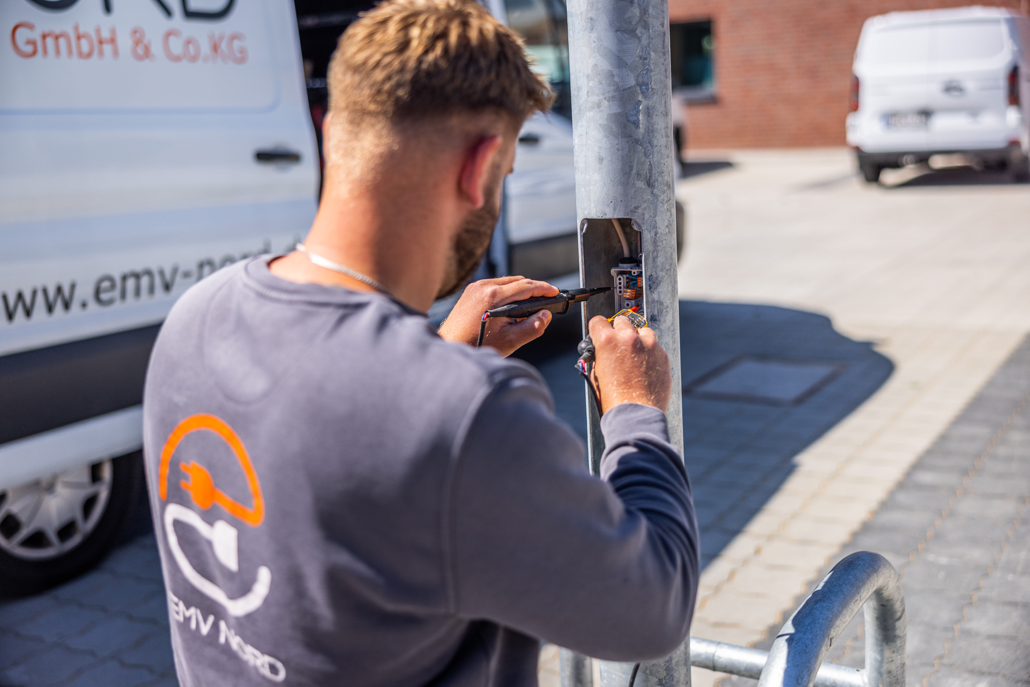Elektriker repariert elektrische Kabel an einem Metallpfosten im Freien bei Tageslicht.