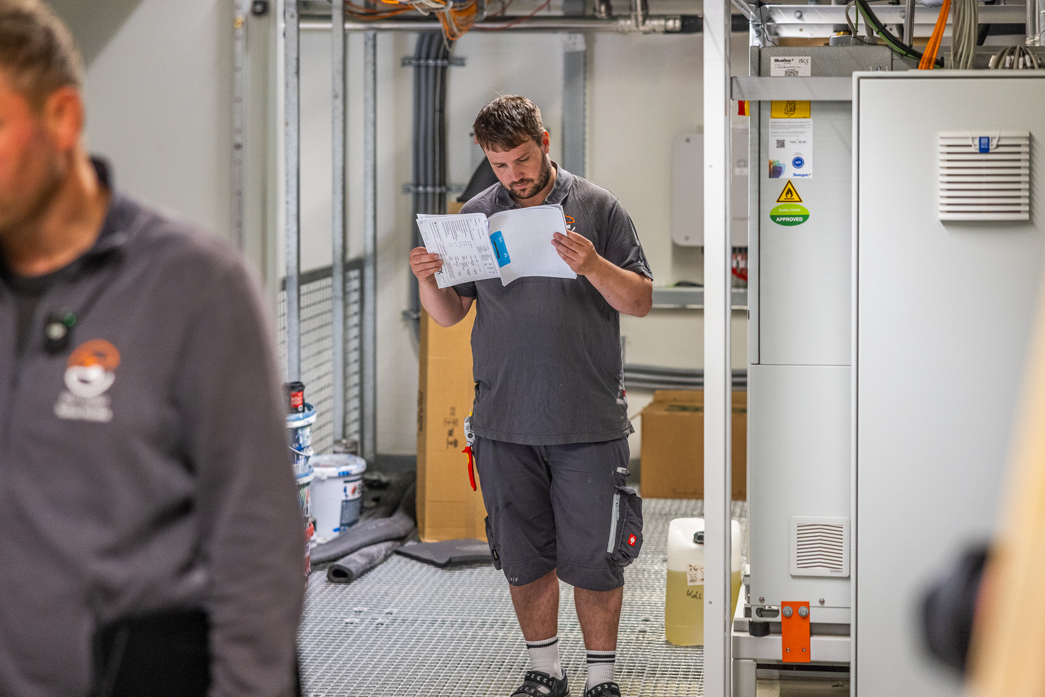 Ein Arbeiter liest ein Dokument in einem technischen Raum mit Gerätschaften und Ausrüstung.