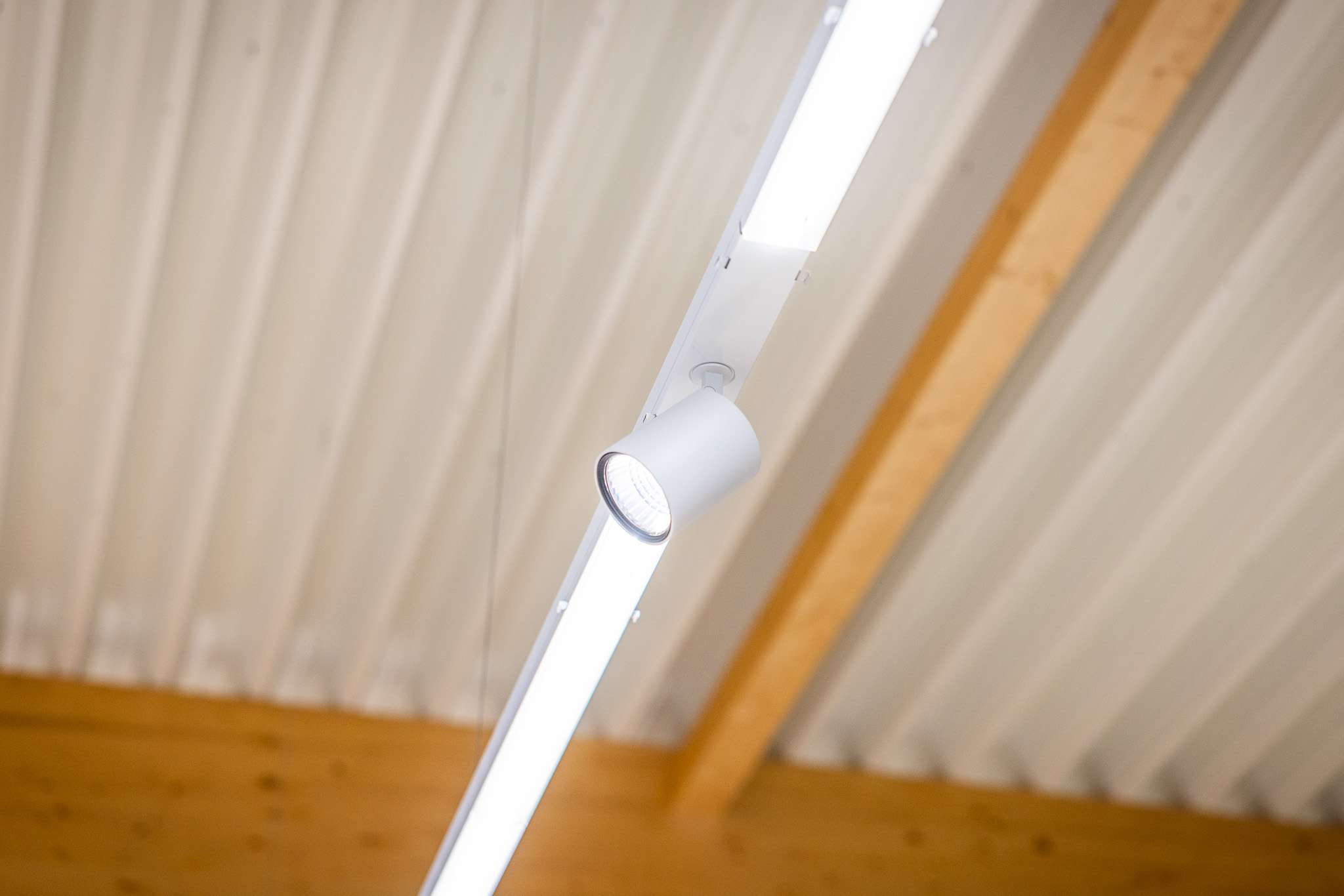 Bürolampe mit aufgehängtem, langem Leuchtstreifen und Spot an einer Decke mit Holzbalken.