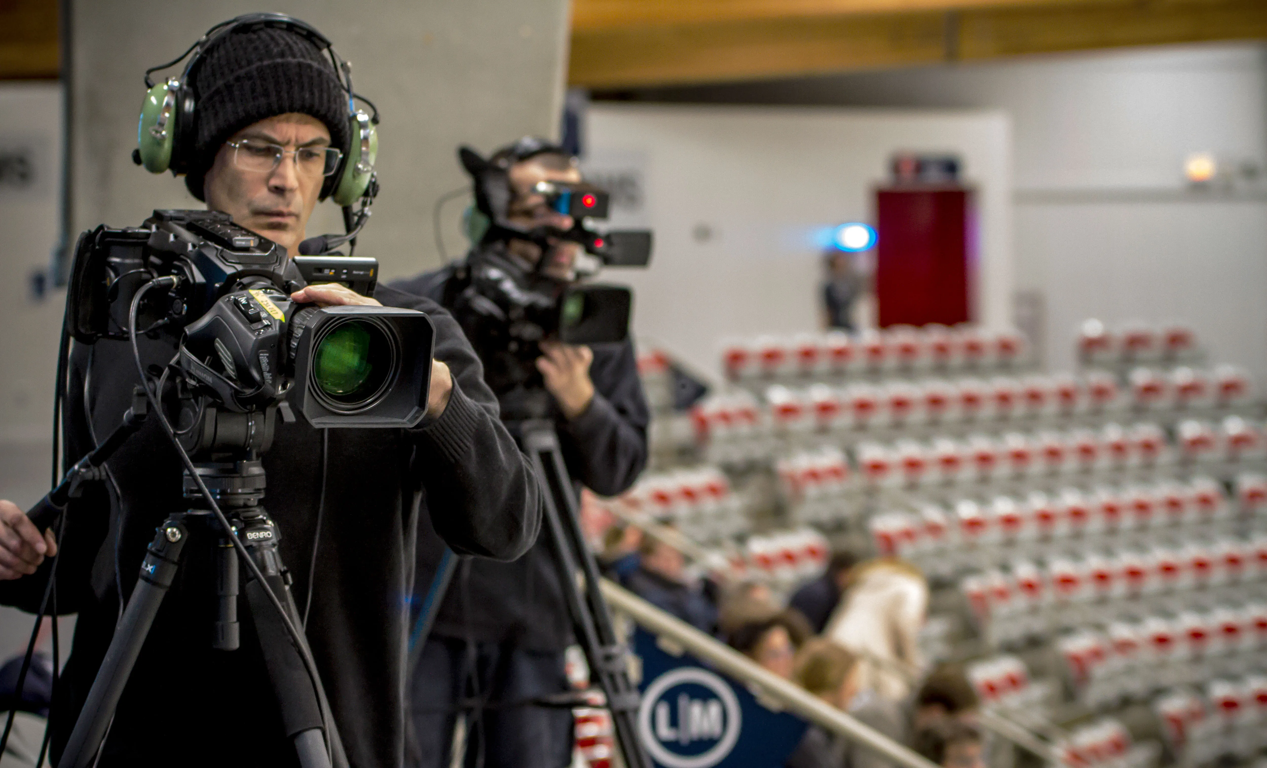 a cameraman wearing large headphones is focused on filming the hockey game