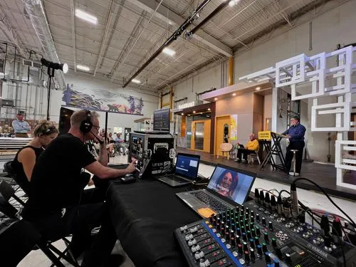 a man wearing large headphones sits behind a table to control AV for the show