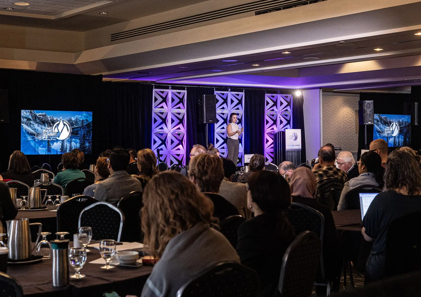 A speaker presenting on stage with blue and purple lights