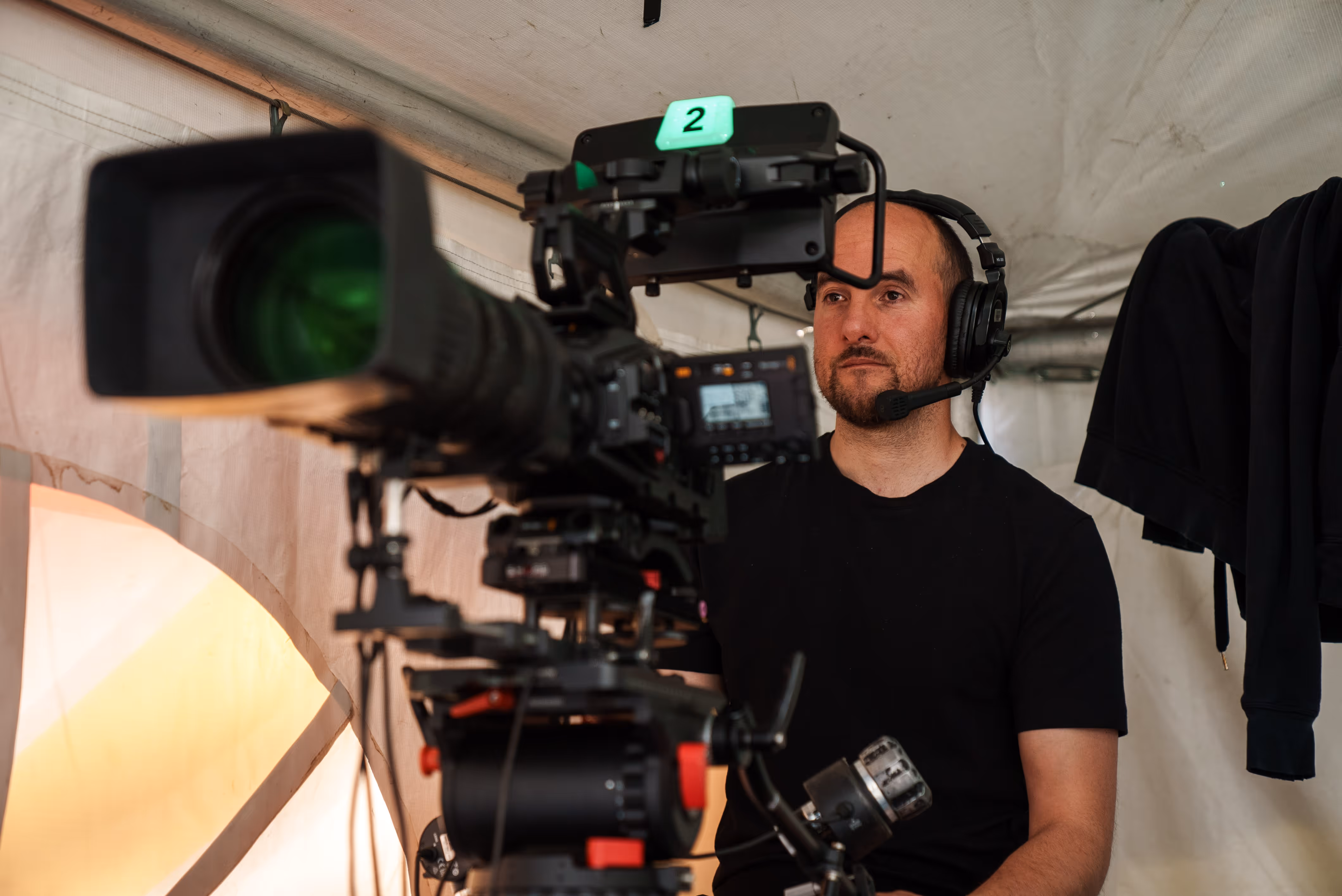 Man wearing headset operating a professional video camera indoors with beige tent-like walls.