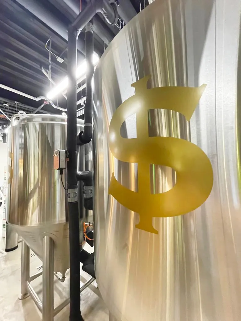 Close-up of large metal tanks with a gold dollar sign on one in an industrial setting.