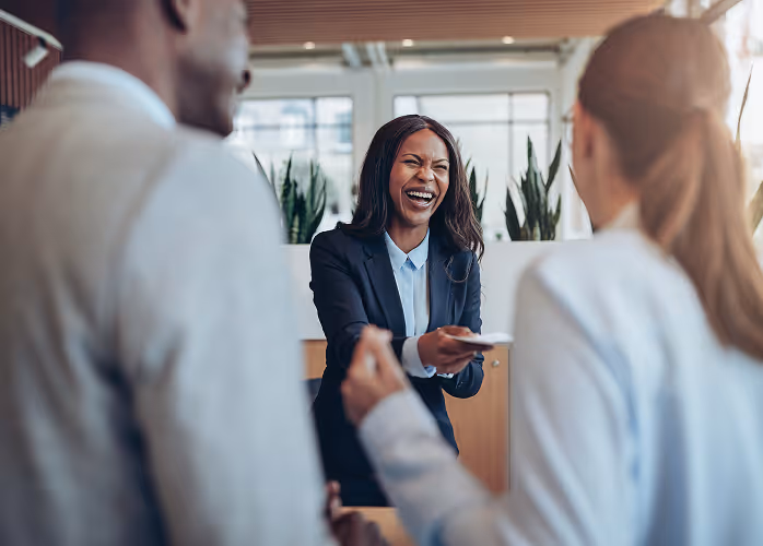 Smiling businesswoman handing a card to two colleagues in an office setting.