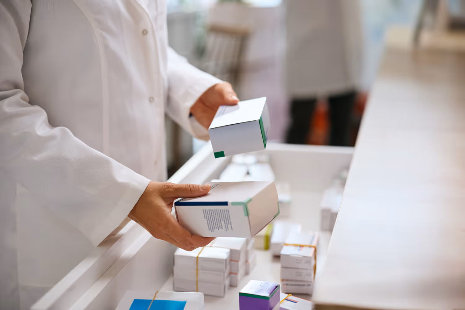 Pharmacist in white coat selecting medicine boxes from a drawer filled with various medications.