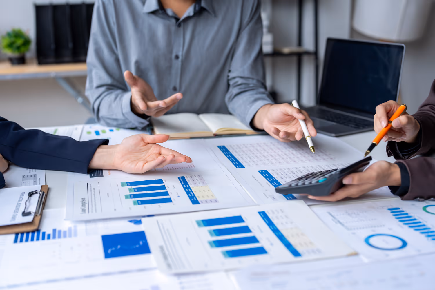 Three people analyzing financial charts and graphs on a table with a laptop and calculator.