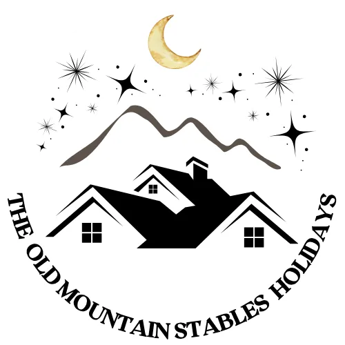 Logo featuring stylized house roofs with windows under mountain peaks, a crescent moon and stars above, with text 'THE OLD MOUNTAIN STABLES HOLIDAYS' in a circle around the image.