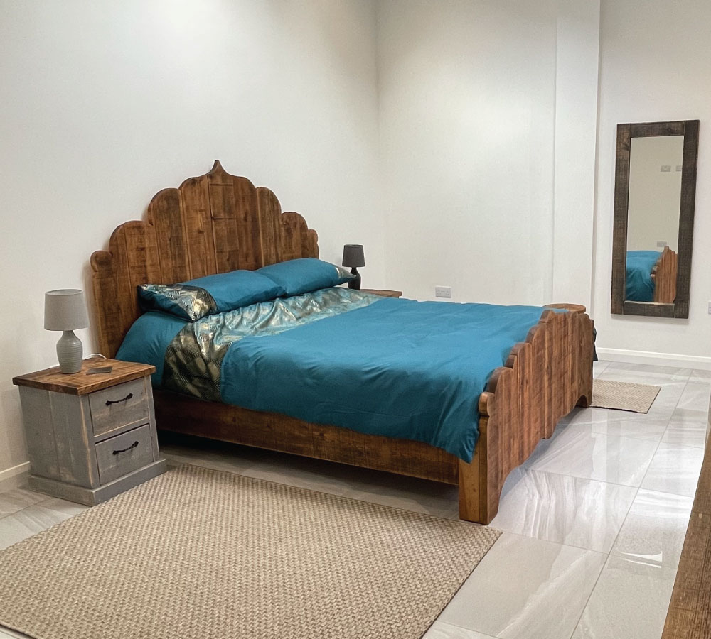 Bedroom with wooden bed featuring blue floral bedding, matching curtains, wooden furniture, and a patterned area rug.
