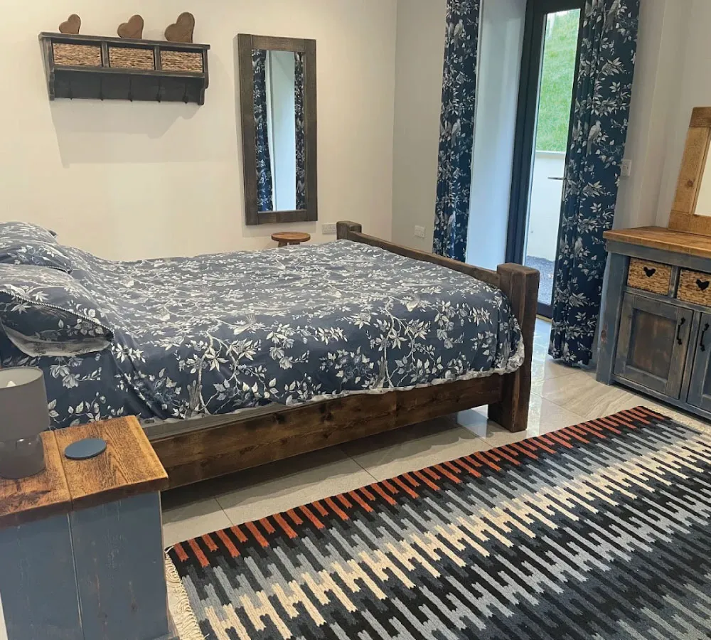 Bedroom with wooden bed featuring blue floral bedding, matching curtains, wooden furniture, and a patterned area rug.