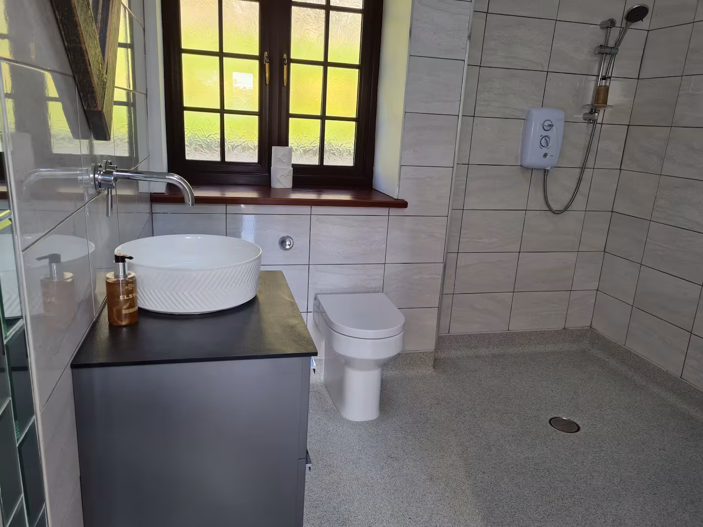 Modern bathroom with white round vessel sink on black countertop, wall-mounted faucet, white toilet, and walk-in shower with handheld showerhead.