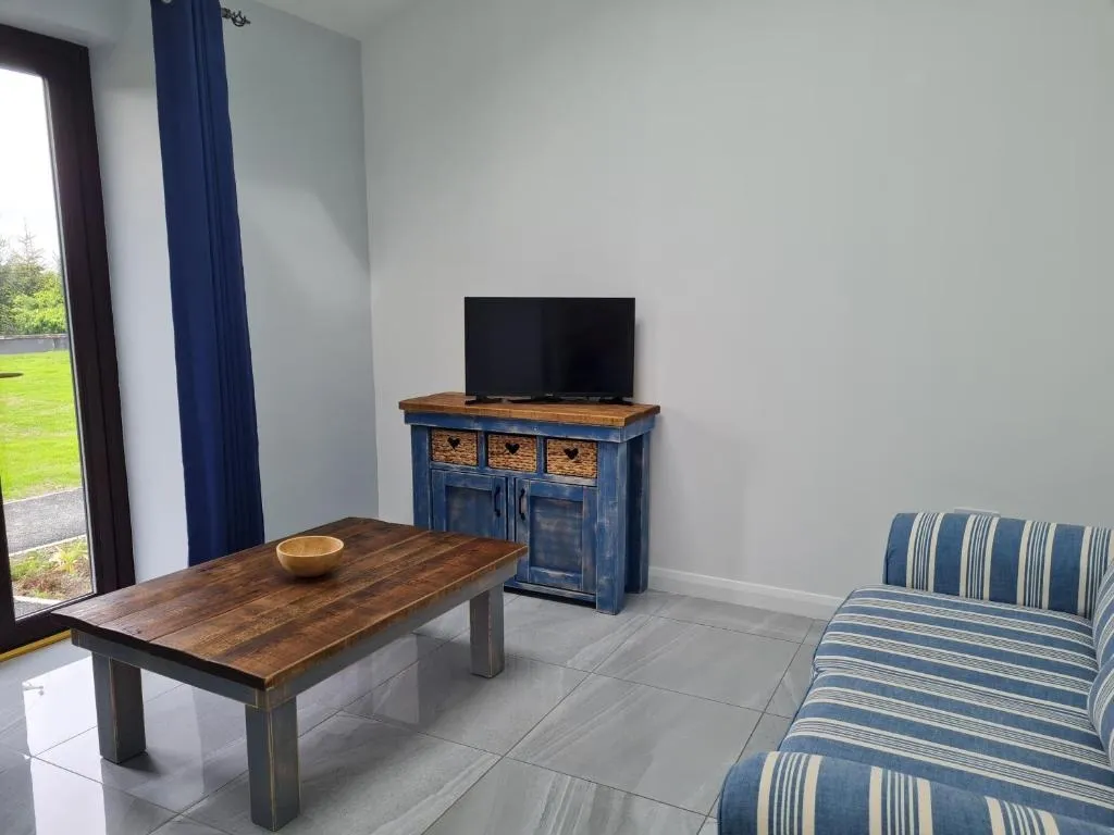 Living room with a blue and striped sofa, wooden coffee table with a bowl, blue cabinet with a TV, and large window with blue curtains.