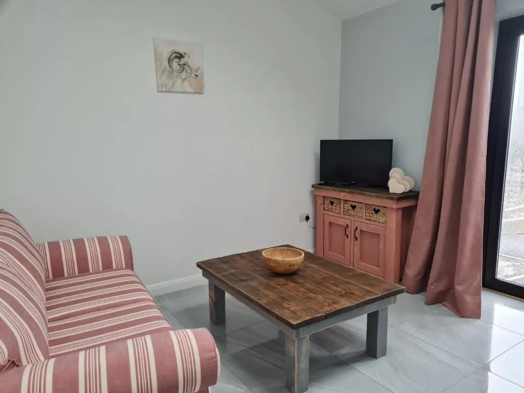 Living room with a red and white striped sofa, wooden coffee table with a wooden bowl, small cabinet with a TV, and pink curtains by a glass door.