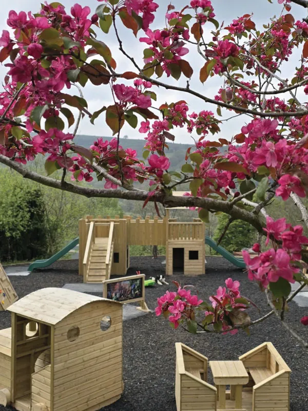 Play area with wooden play structures and tables, framed by pink flowering branches.