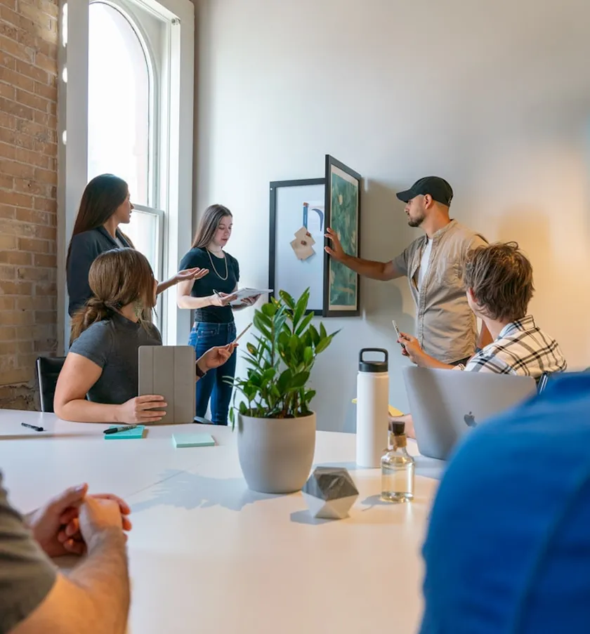 Atelier en petit groupe : un intervenant présente un tableau accroché au mur à des participants réunis autour d'une table