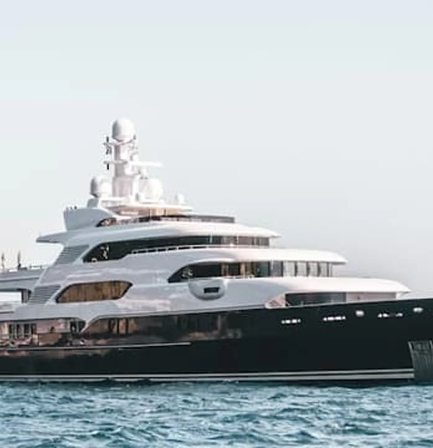 Illuminated luxury superyachts docked at a marina during sunset with clear sky.