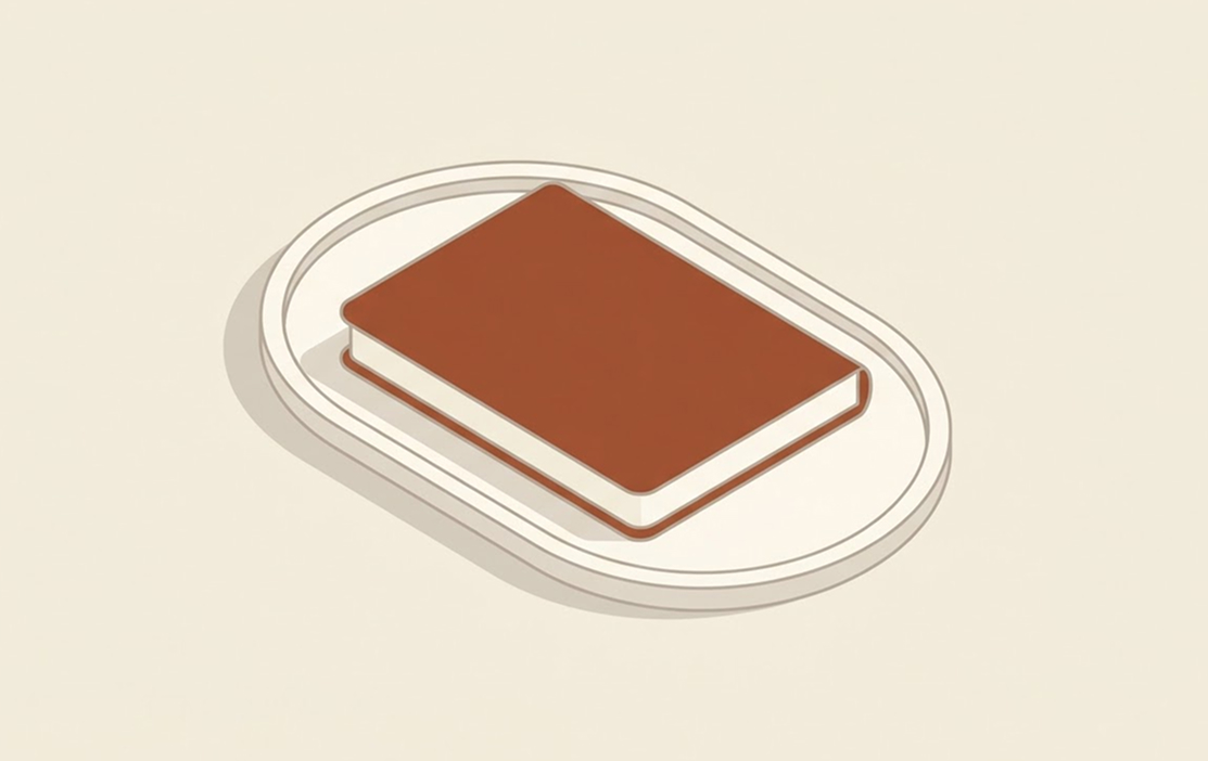 Illustration of a closed brown hardcover book placed on a white oval-shaped tray casting a shadow on a light beige background.