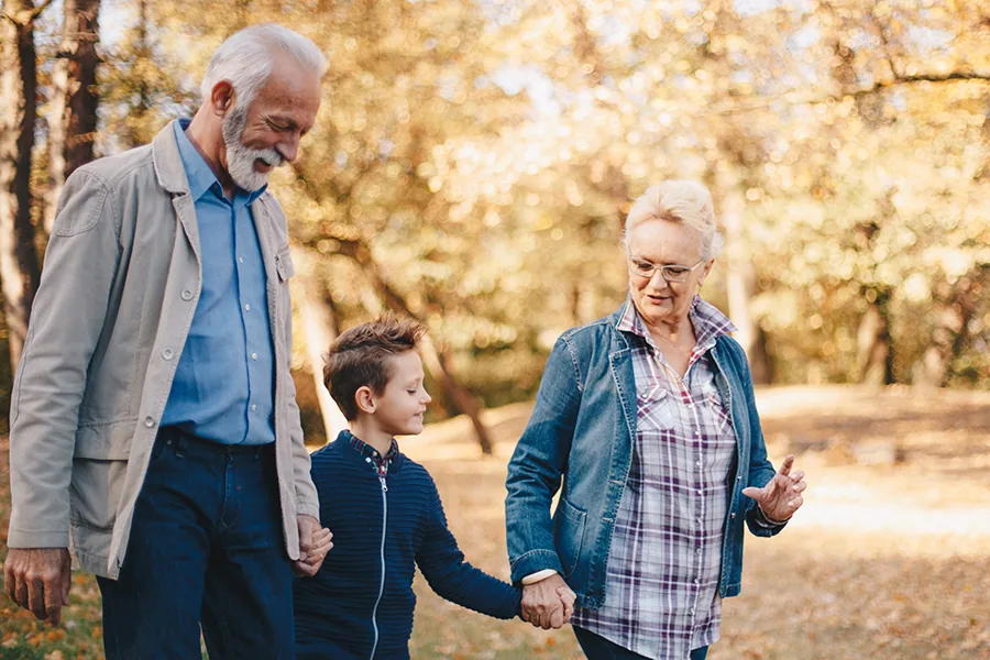 Elderly couple walking outdoors in autumn holding hands with their grandson between them.