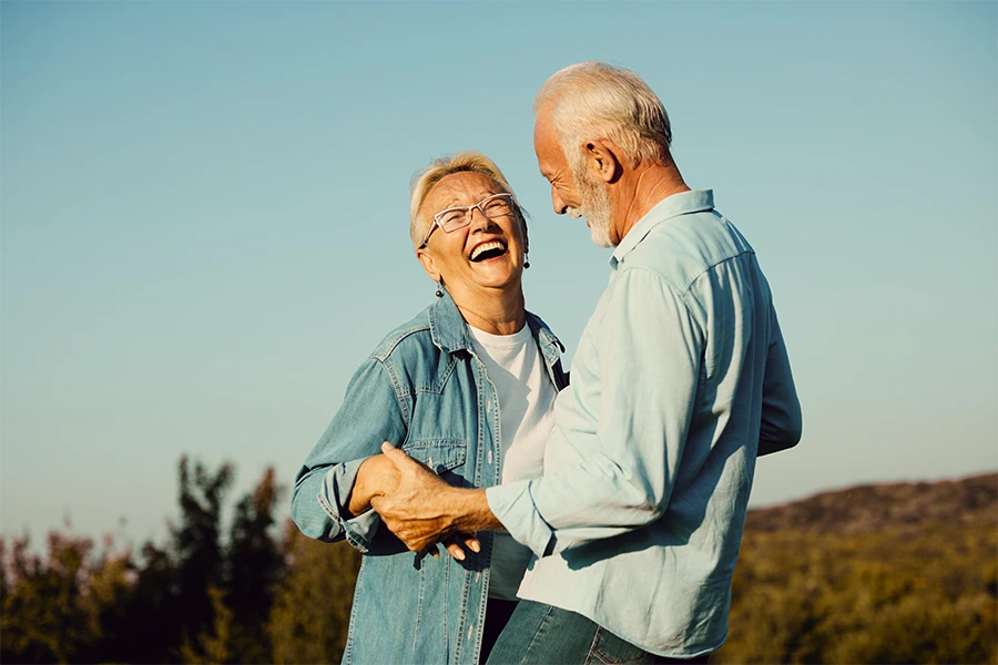 Happy senior couple holding hands and laughing outdoors under a clear sky.