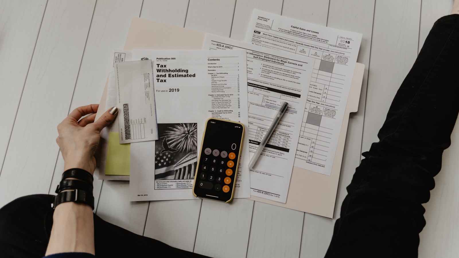 Hands sorting tax forms with a phone calculator