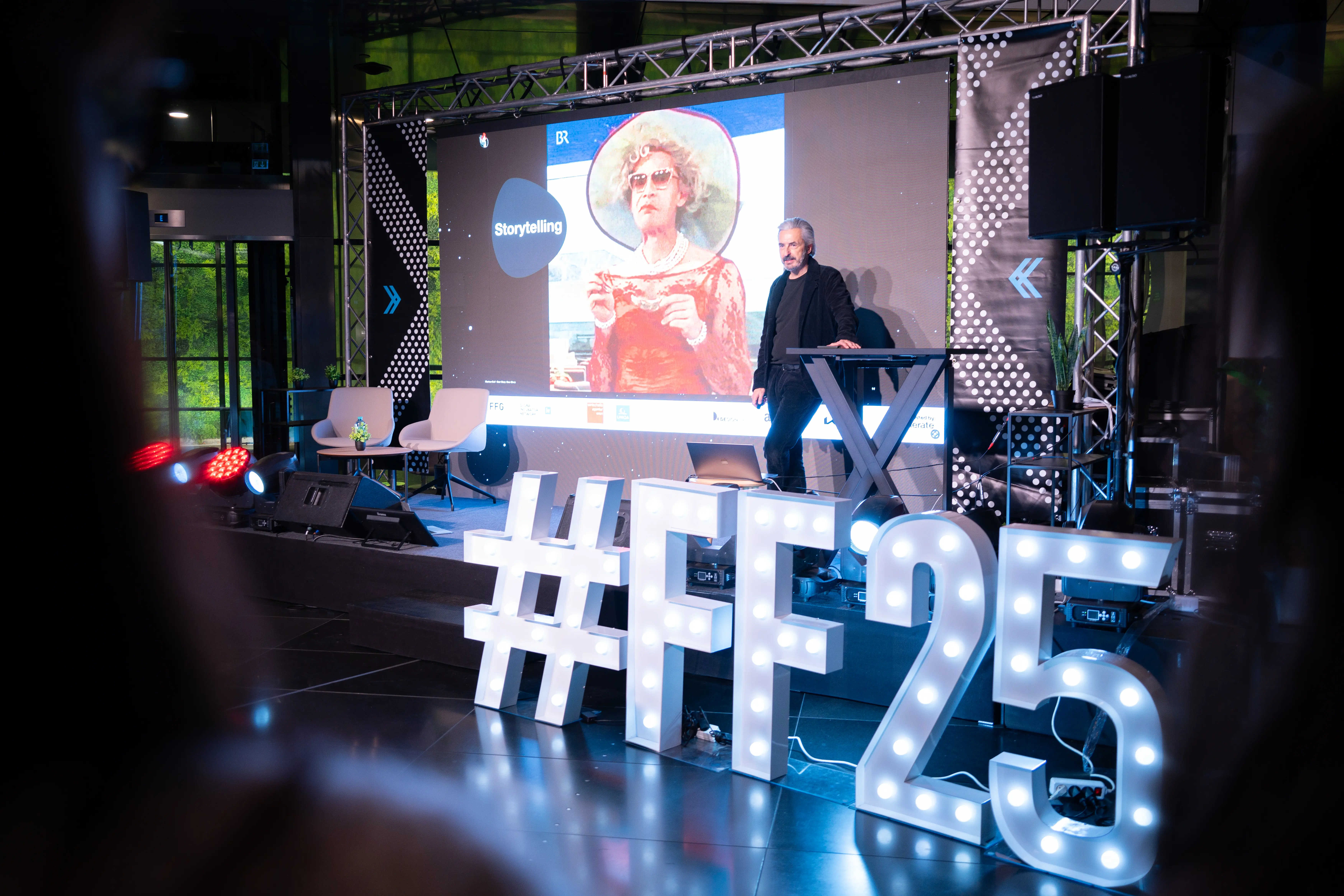 A speaker on stage beside a Storytelling slide, with large lit-up #FF25 letters and a silhouetted Future Forward audience in the foreground