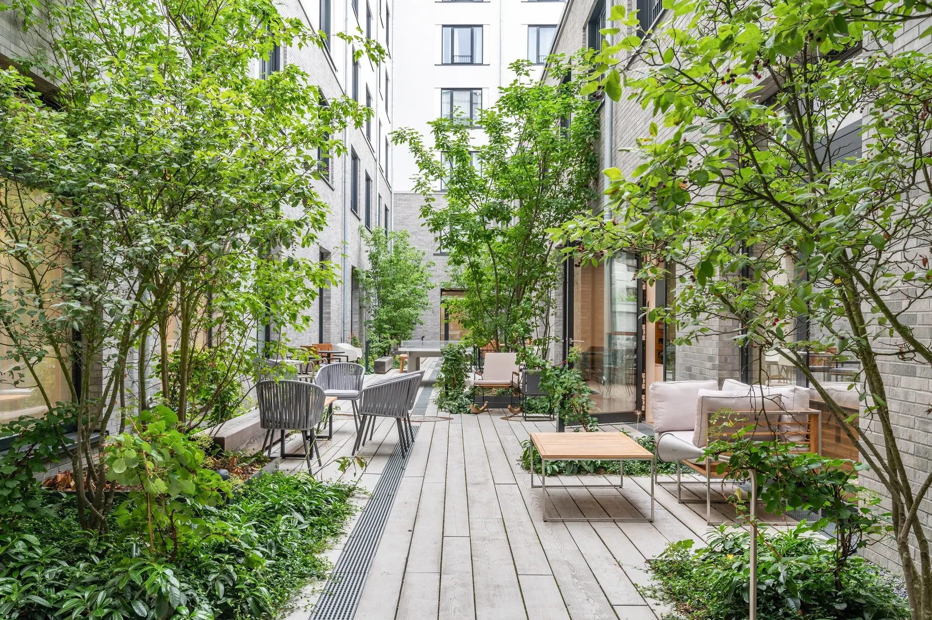 Begrünter Innenhof des Habyt Berlin Waterfront mit Holzdeck, Bäumen und Sitzgruppen