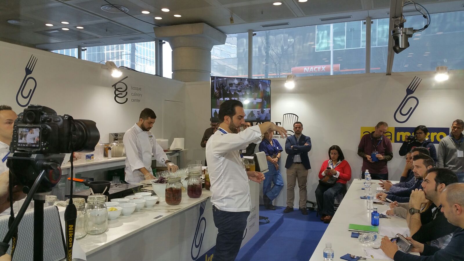 Un chef haciendo una demostración de cocina en directo en un stand de Madrid Fusión en 2017, con asistentes sentados tomando notas y fotógrafos grabando