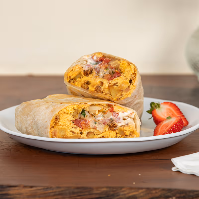 Two halves of a burrito filled with scrambled eggs, chorizo, potatoes, and sauce on a white plate garnished with sliced strawberries.