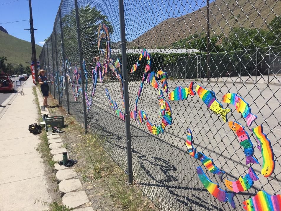 A chain-link fence decorated with a "stream" of brightly painted wooden fish, created by community members to raise awareness for watershed health.