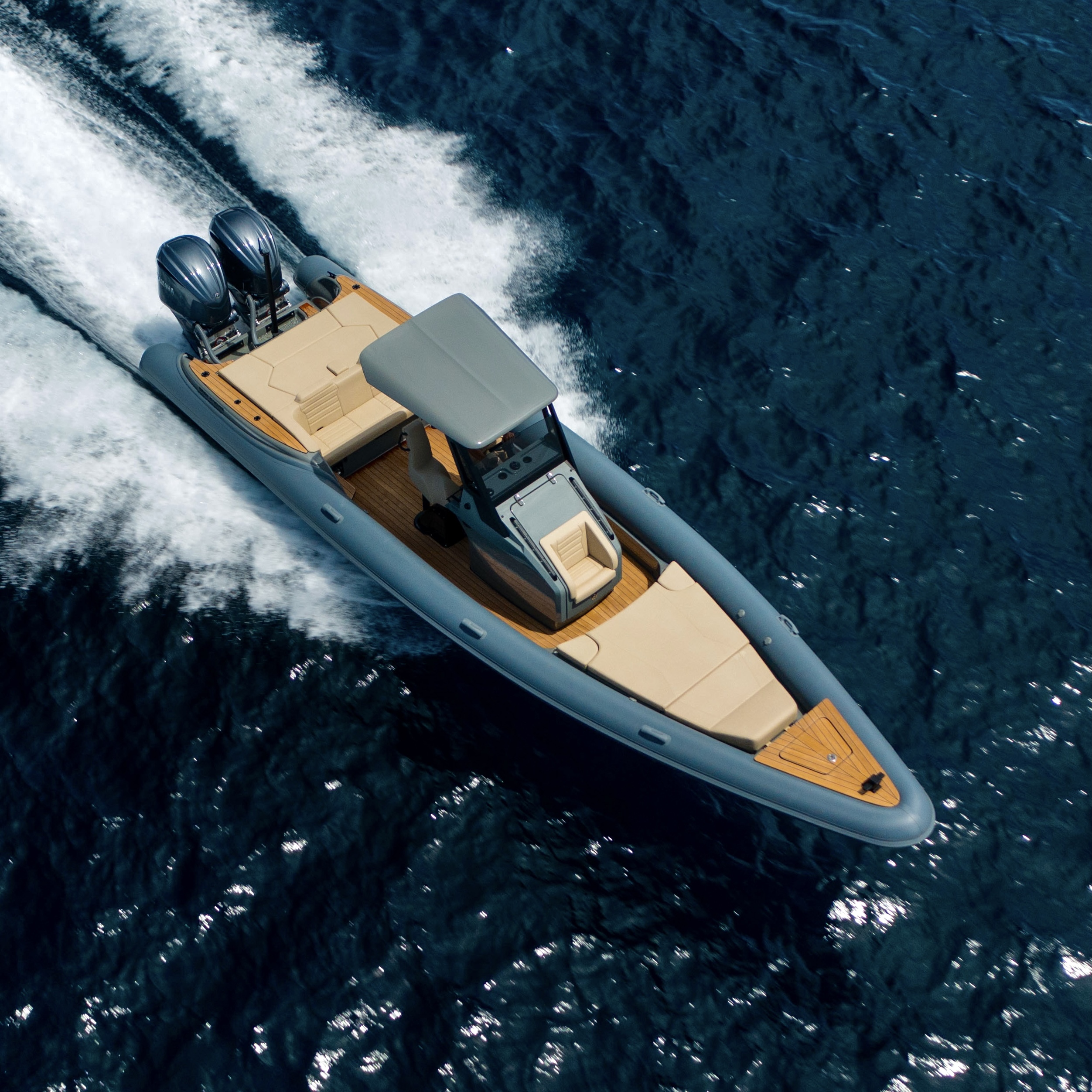 A sleek, gray motorboat with beige seating glides through deep blue water, leaving a white wake behind.