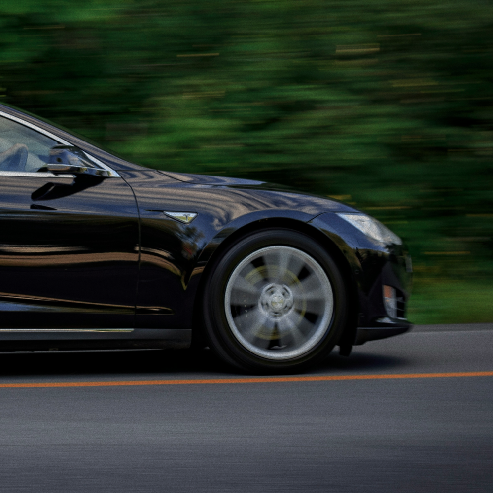 Close-up of a black electric car in motion on a road with blurred green foliage background.
