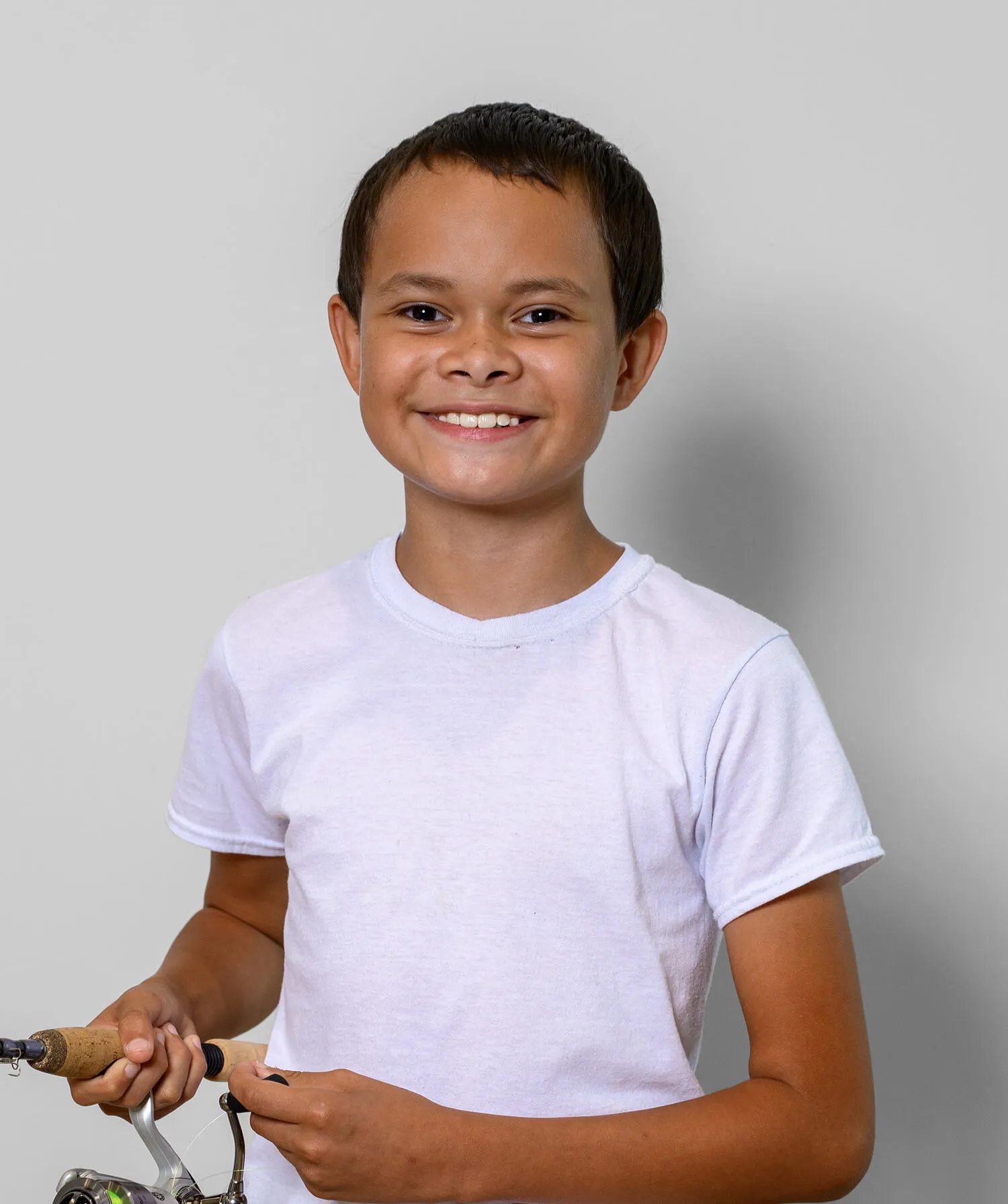 Smiling boy in a white t-shirt holding a fishing rod against a plain background.