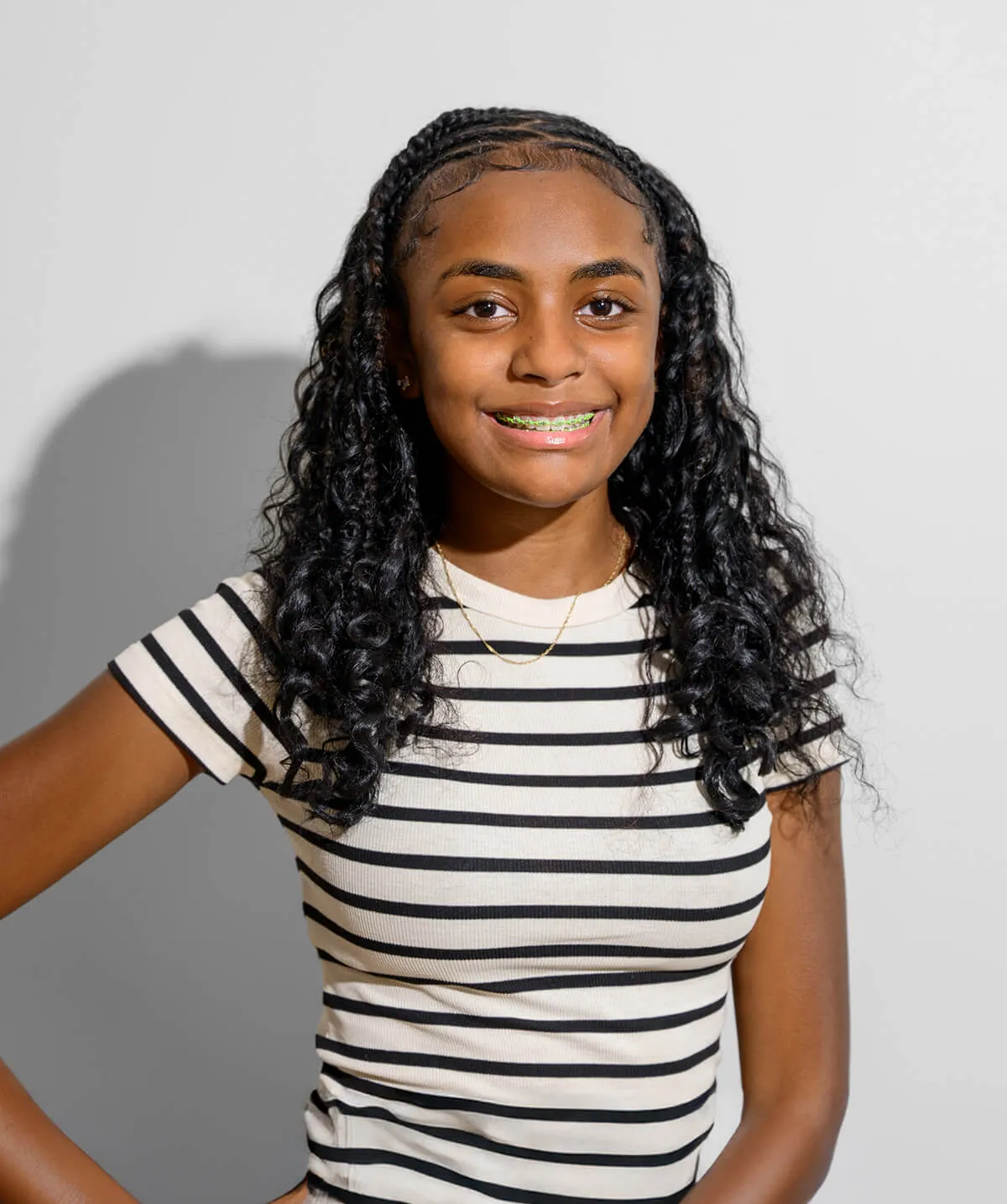 Smiling young woman with curly hair and braces wearing a black and white striped shirt.